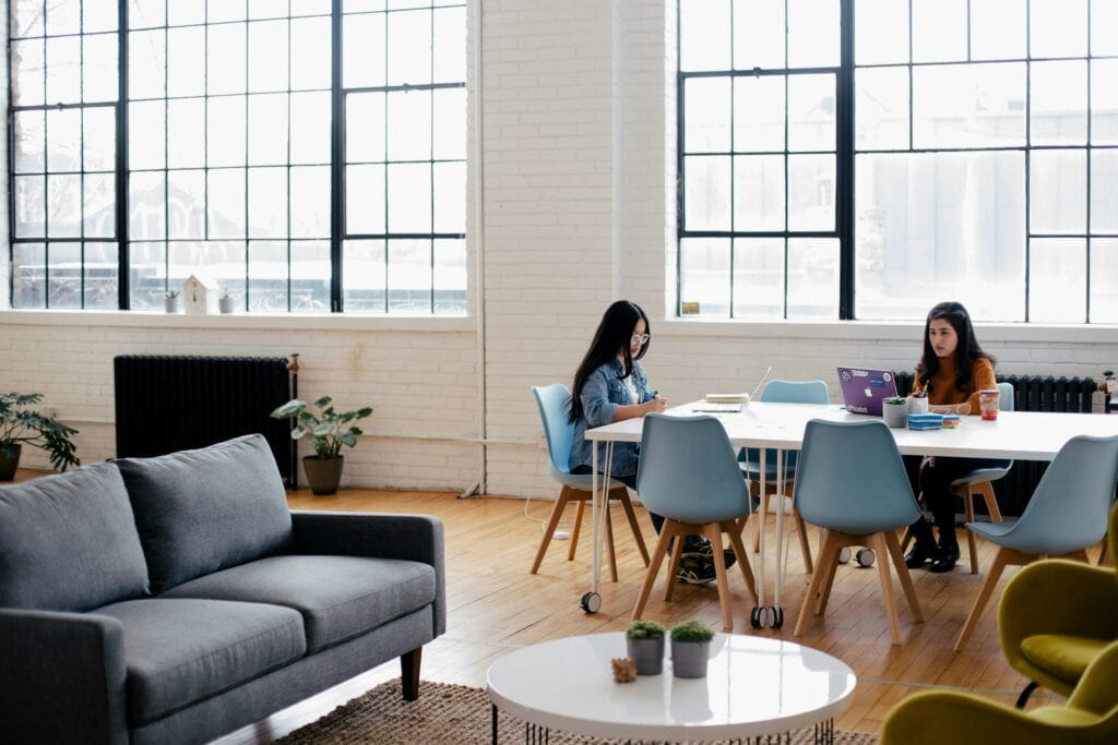 Two women sitting at laptops at a big table reviewing the company AI policy.