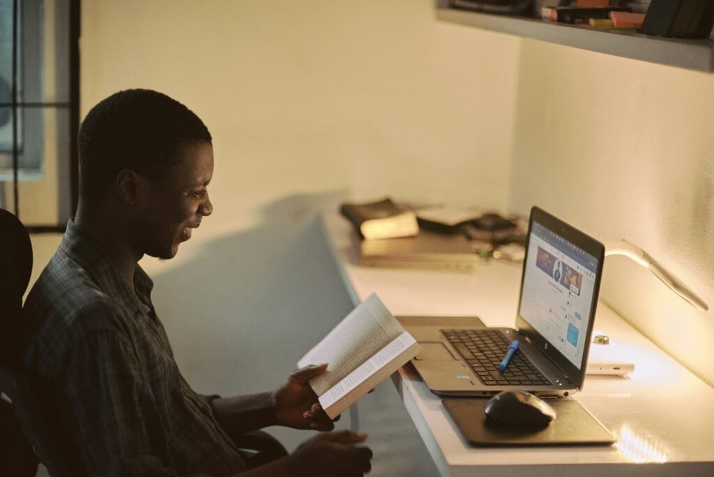 Man studying at a table with a book and a laptop as part of employee upskilling program.