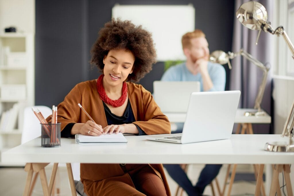 Woman sitting at a desk writing on a pad about the importance of communication skills.