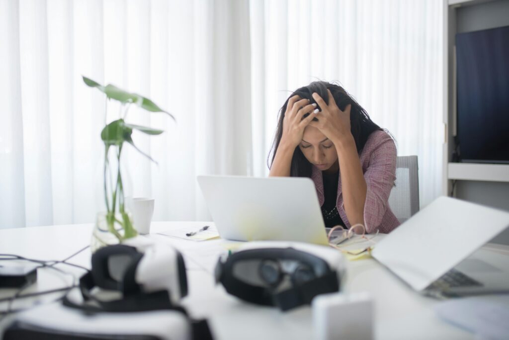 Woman sitting in front of laptop at desk with her head in her hands.