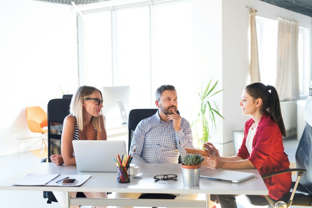 Three HR managers sitting around a table at their laptops discussing AI hiring fraud.