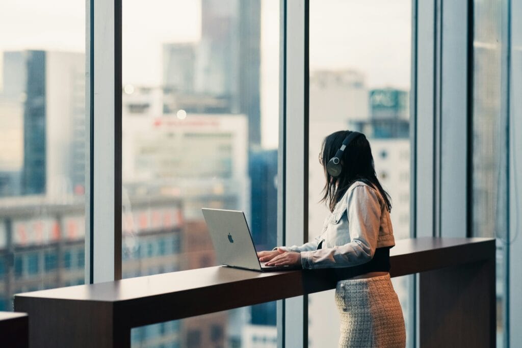 Woman standing at a laptop looking out window.