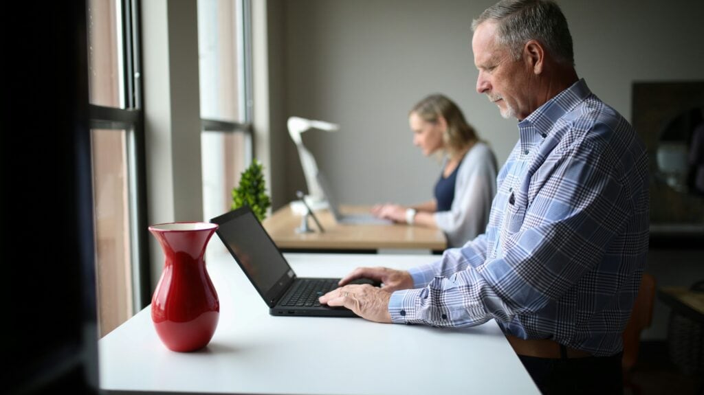 A man standing at a desk on his laptop using AI reference checks.