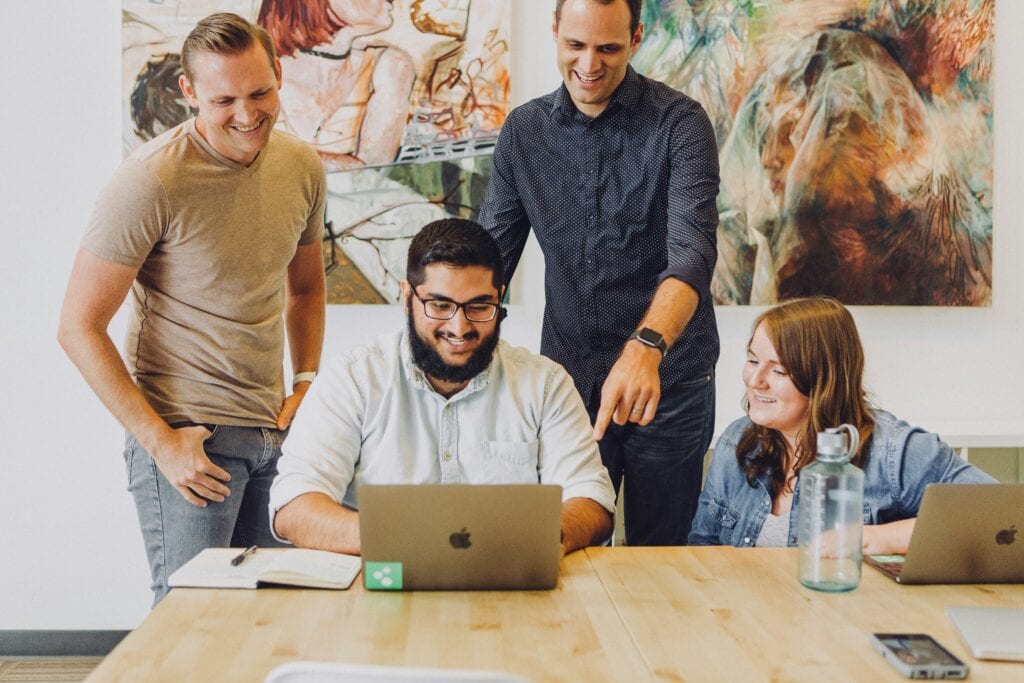 A group of employees standing around a laptop discussing predictive hiring data.